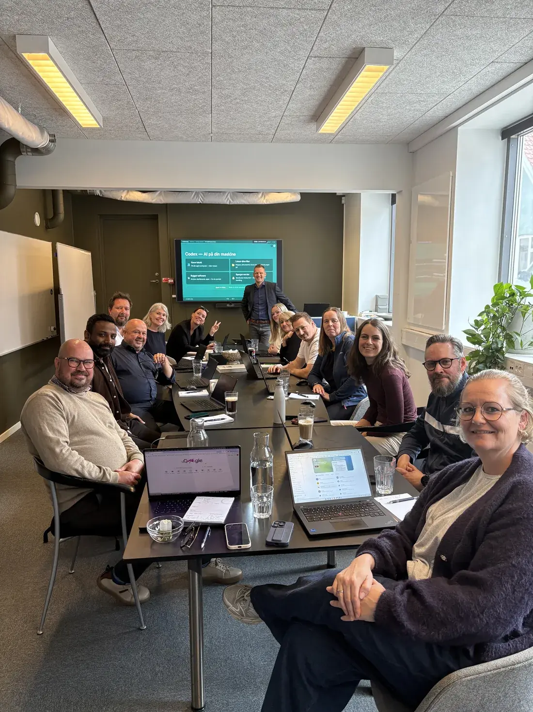 Brian underviser et hold medarbejdere i AI på en workshop, alle med laptops fremme